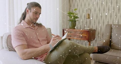 Man sketching in notebook on sofa with digital network overlay, midcentury living room