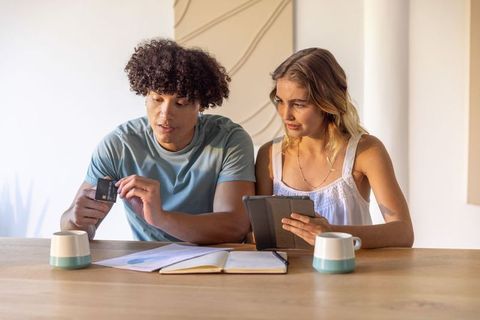 Young couple budgeting and reviewing finances with tablet and credit card in sunlit kitchen