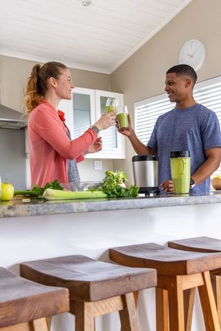 Couple toasting green smoothies in sunlit kitchen preparing healthy morning ritual