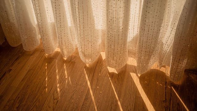 Sheer Dotted Curtain Casting Warm Sunbeams Over Hardwood Floor with Patterned Shadows