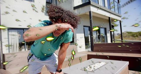 Curly-haired man shielding face from glowing green fragments on modern patio