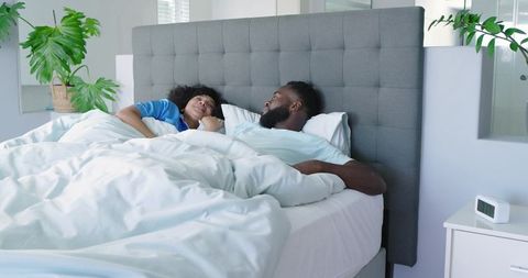 Diverse couple relaxing together in bright modern bedroom with tufted headboard