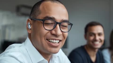 Close-up smiling professional wearing glasses and earbud responding in team meeting video