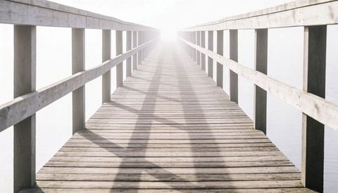 Wooden pier leading toward bright horizon over calm lake, high-key minimalist boardwalk