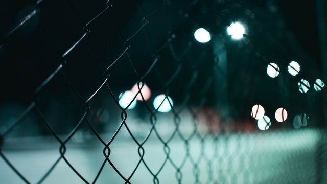 Close-up shot of a chain-link fence at night with bokeh from city lights in the background. This image evokes themes of boundaries, isolation, and urban environments. Ideal for use in articles about urban life, security, night photography, or as a metaphor for barriers and separation.