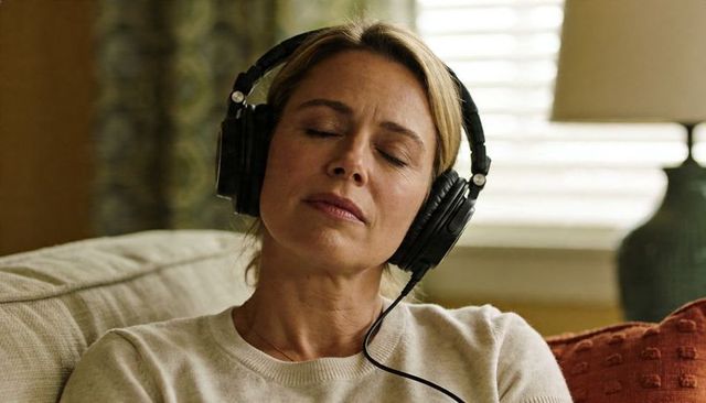 Middle-aged woman relaxing with wired headphones on sofa, eyes closed, cozy listening