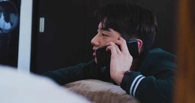 Asian male teenager talking on smartphone and lying in living room. spending time alone at home.