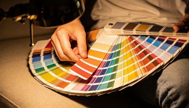 Designer holding color swatch fan selecting warm red and neutral palettes for upholstery