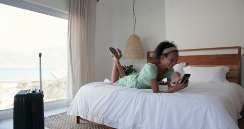 African American Woman Relaxing in Seaside Bedroom with Smartphone