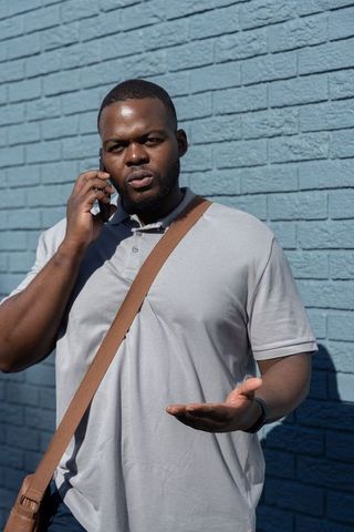 African american man making phone call and gesturing against blue brick wall in daylight