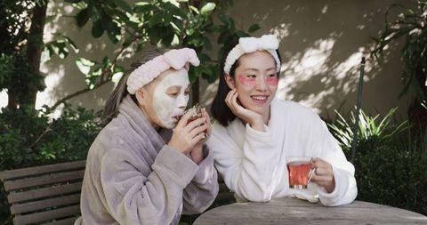 Mother and Daughter in Robes Enjoying Tea With Skincare Masks Outdoors