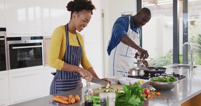This vibrant image of a joyous African American couple cooking together in a stylish kitchen can be ideal for illustrating blog posts or articles about relationships, home life, and cooking experiences. It may also be perfect for use in online media or print materials promoting family bonding, culinary courses, and modern lifestyle. Additionally, it suits advertising campaigns for kitchen appliances, food ingredients, or lifestyle products.