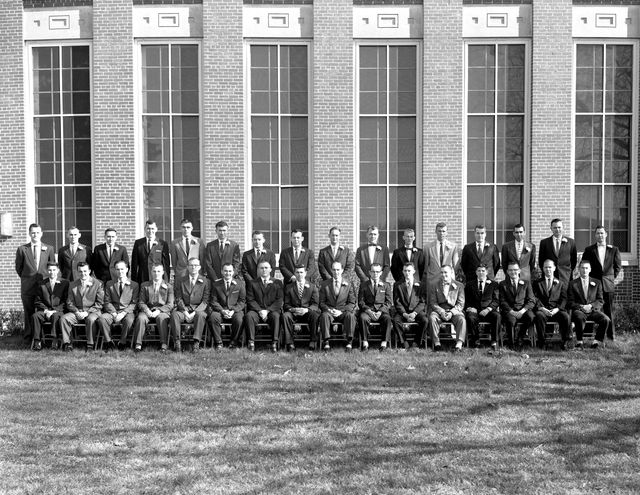 A group of 32 apprentice graduates poses in front of a building wearing formal attire. This historic black and white photo portrays a class completion event, making it suitable for historical articles, educational resources, or visuals related to professional training and graduation ceremonies.