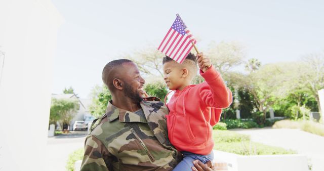 Happy african american father with son embracing and waving flag of usa. Global patriotism and family concept.
