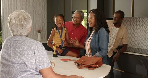 Multigenerational family celebrating child winning trophy on marble kitchen island