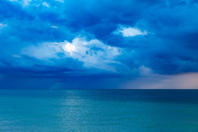 Photo captures dramatic sky with heavy clouds over calm ocean waters during sunset. Ideal for use in travel brochures, nature-inspired designs, desktop wallpapers, and meditation apps to convey serenity and natural beauty.