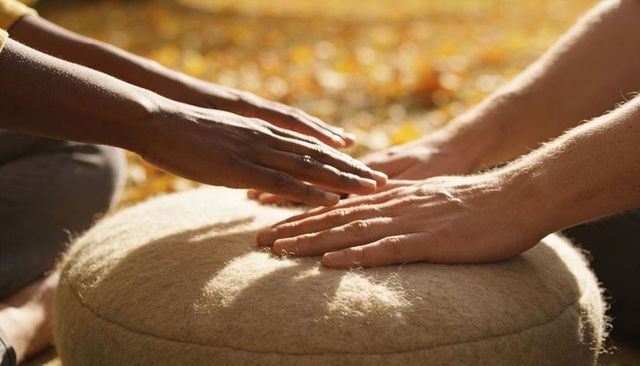 Two pairs of hands pressing wool cushion in autumn sunlight at park