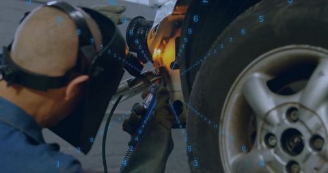 Automotive Welder Repairing Car Body Panel Near Wheel with TIG Torch and Safety Helmet