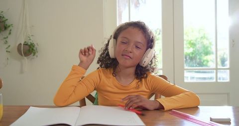 Curly-haired girl studying with headphones, tapping notebook and enjoying music