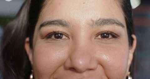 Closeup portrait showing woman smiling, gold hoop earrings, natural skin texture, makeup