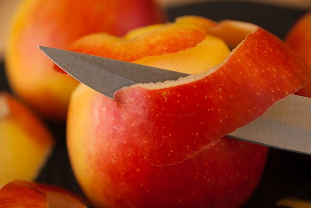 Close-up showing knife slicing red apple, capturing the freshness and vivid color. Ideal for use in food blogs, healthy eating articles, recipe books, or advertisements focusing on fresh produce and culinary skills.