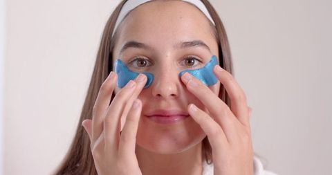 Woman using blue gel eye patches for skincare routine