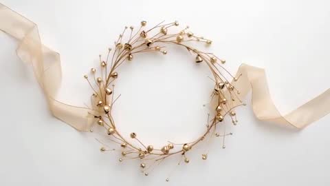 Slow-moving golden wreath with flowing sheer ribbon and tinkling beads on white surface
