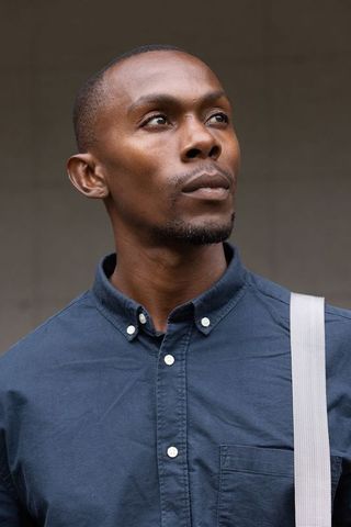 Contemplative african man headshot wearing navy button-down shirt with white strap neutral backdrop