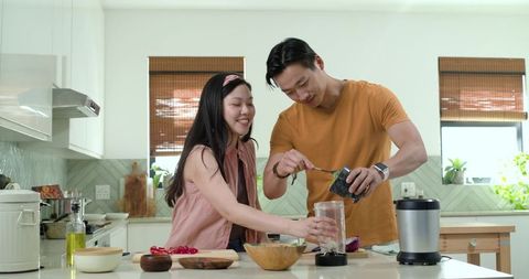 Couple making green smoothie together in bright modern kitchen for healthy lifestyle