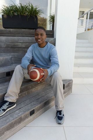 African american teen sitting on porch holding football smiling casual modern lifestyle