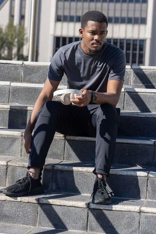 African american man resting on concrete steps holding headphones and checking fitness watch