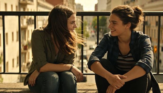 Chatting friends on urban rooftop railing with warm sunlight and casual denim