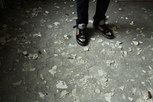 Person is seen standing on a floor covered with peeling paint and debris. The floor has hexagon tiles, giving an old, abandoned look to the place. The image can be used in contexts related to urban exploration, decay, or depicting the passage of time. It is also useful for themes of neglect, forgotten places, or as a background for various editorial concepts.