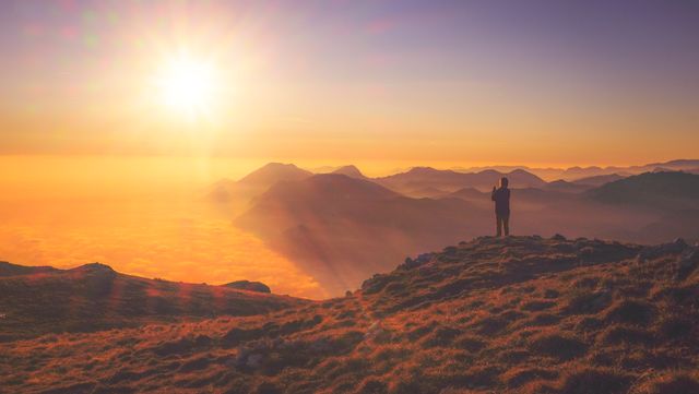 Silhouette of person standing on mountain peak during sunrise, overlooking misty valleys. Suitable for use in travel brochures, inspirational content, and nature blogs promoting adventure and outdoor activities.