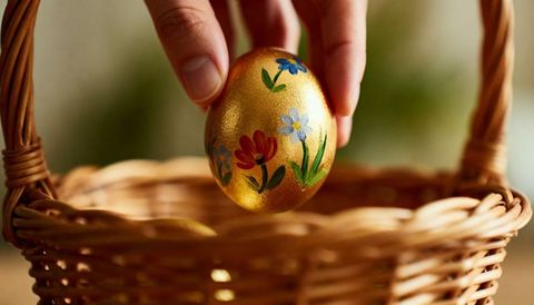 Hand placing painted golden egg into wicker basket with floral motifs for easter
