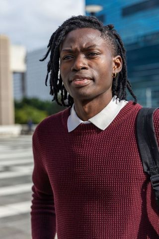 African american professional on city crosswalk wearing burgundy sweater and backpack