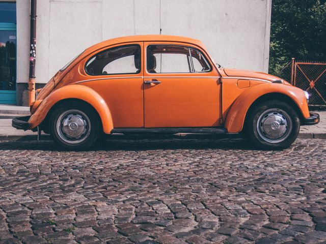 Parking vintage orange Beetle on cobblestone street creates a retro vibe. Perfect for retro-themed campaigns, automobile clubs, or nostalgic visual content showcasing classic vehicles. Useful for reminiscing about past eras or adding a vintage touch to modern projects.