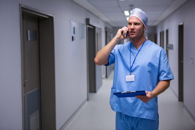 Surgeon standing in corridor and talking on mobile phone in hospital