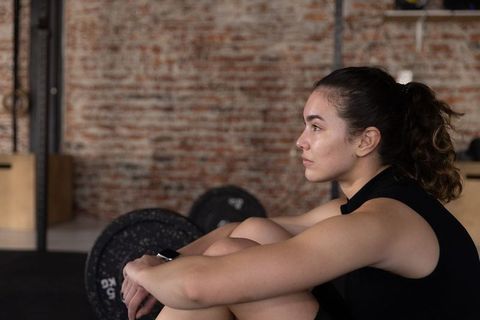 Female athlete resting between sets in industrial gym with barbell and focused gaze