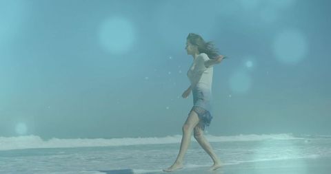 Woman walking barefoot along teal beach shoreline with lens flare and bokeh light effects