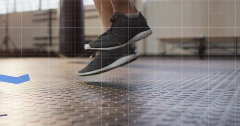 Jumping athlete feet hovering over studded gym floor with dark sneakers, daylight windows