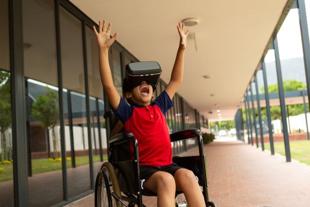 Young biracial boy sitting in a wheelchair, using a virtual reality headset at school. He is wearing a red shirt and black shorts, raising his hands in excitement. This image can be used for promoting inclusive education, showcasing the use of technology in learning, or highlighting the joy and engagement of children with disabilities.