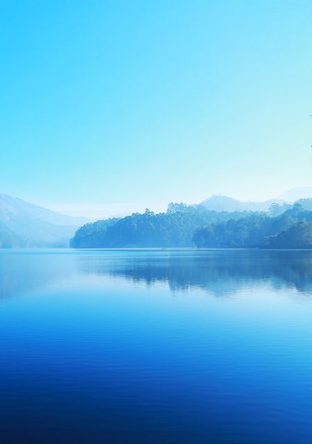 Peaceful scene of a tranquil mountain lake at dawn with perfectly still water creating a mirror-like reflection. The blue hues emphasize the calm and serene nature of the landscape. Ideal for use in travel blogs, relaxation and meditation content, interior design accents, and nature-inspired publications.