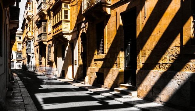 Sunlit stone alley casting diagonal shadows across historic facades and wooden balconies