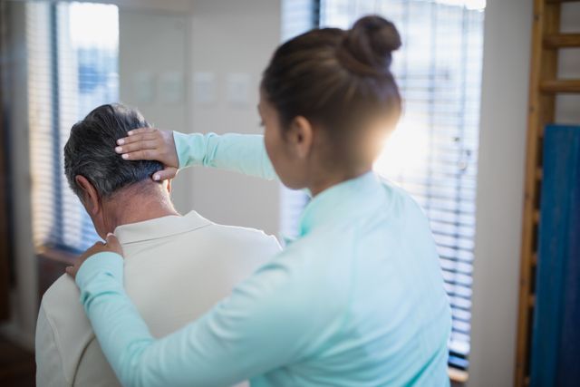 Female therapist providing neck massage to senior male patient in a hospital ward. Ideal for use in healthcare, physical therapy, rehabilitation, and elderly care contexts. Can be used in articles, brochures, and websites related to medical treatment, wellness, and professional care.