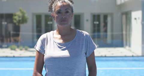 Woman standing on blue court wearing light gray t-shirt in sunlit urban sports space
