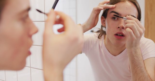 Young adult applying eyeliner in a bathroom mirror. This can be used for topics related to beauty, personal grooming, self-care routines, and cosmetics. Ideal for beauty blogs, skincare articles, and social media content focused on makeup application and personal care.