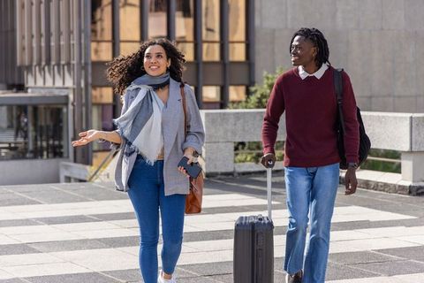 Multiethnic couple walking with suitcase in urban plaza, casual business travel lifestyle