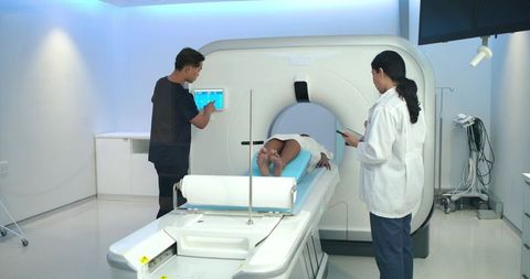 Ct scan technicians monitoring adult patient on scan table in modern radiology suite