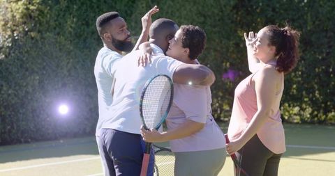 Sunlit tennis players sharing group hug and celebrating victory on grass court